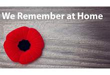 A poppy on the left of the image with a background of a panel of wood. Text at the top reads: We Remember at Home